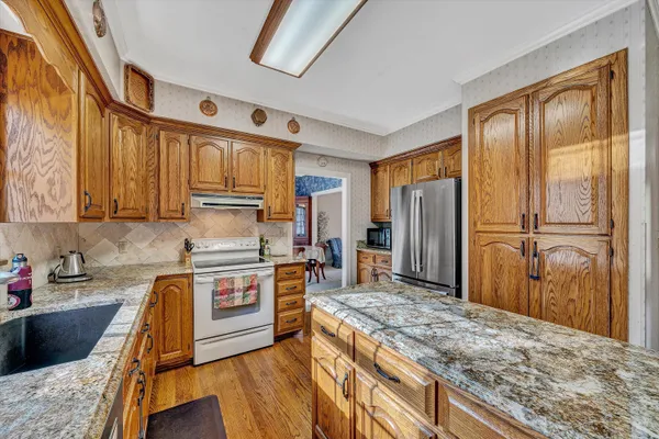 a kitchen with stainless steel appliances granite countertop a refrigerator a stove and a sink with wooden floors