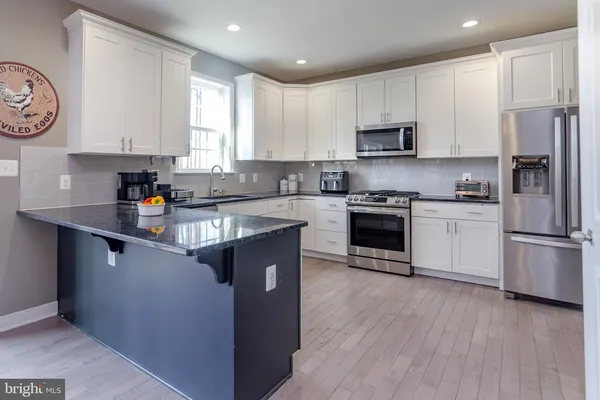 a kitchen with kitchen island granite countertop a refrigerator a stove a sink and white cabinets