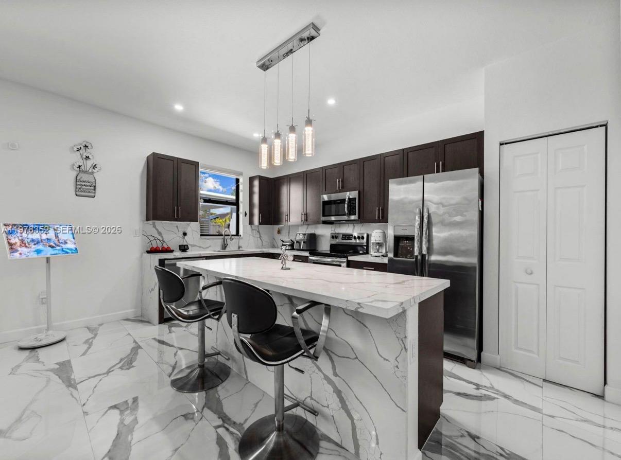 13351 Southwest 190th Street Miami, FL 33177 - Photo 13 of 45 a kitchen with stainless steel appliances kitchen island a table chairs refrigerator and microwave