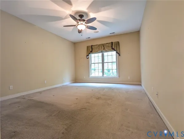 an empty room with chandelier fan and windows
