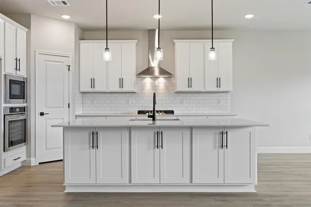 a kitchen with stainless steel appliances granite countertop a sink a refrigerator and white cabinets