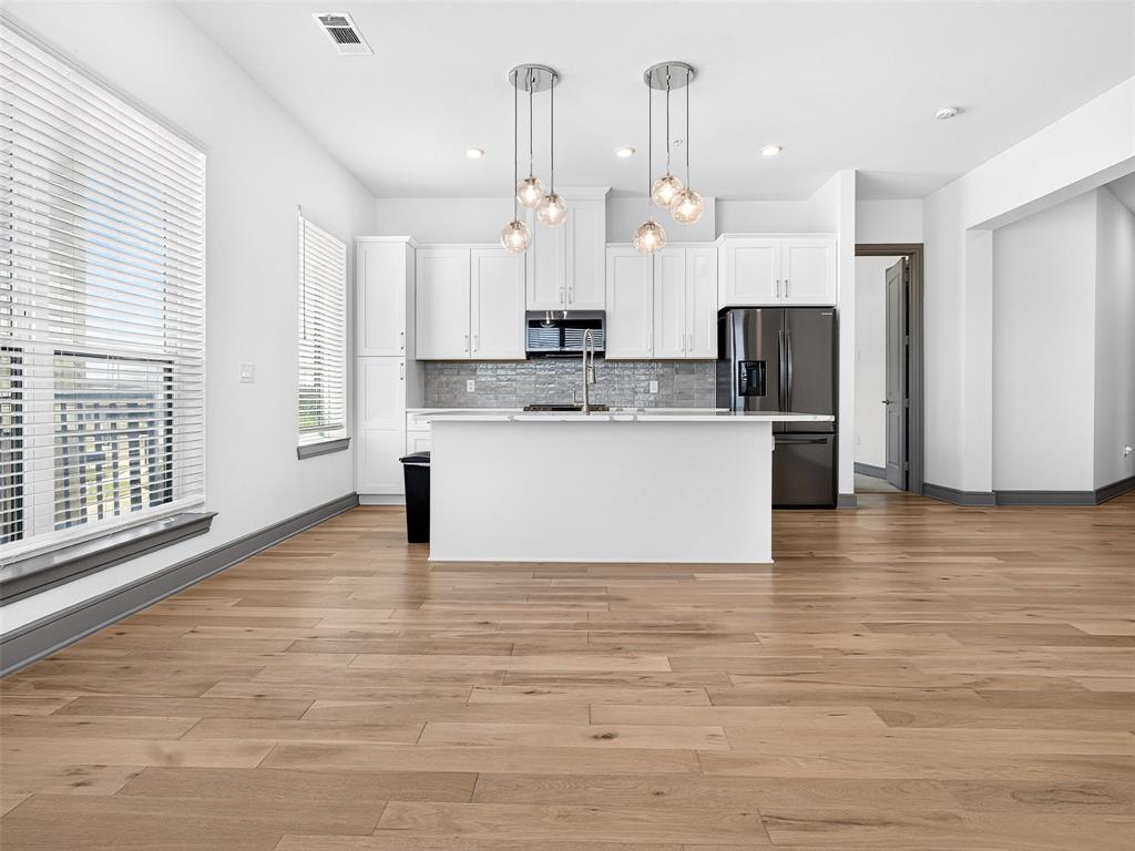 2700 Old Denton Road, Unit 2212 Carrollton, TX 75007 - Photo 13 of 38 Kitchen featuring white cabinetry, a central island, stainless steel appliances, wood-finish flooring, and pendant lighting