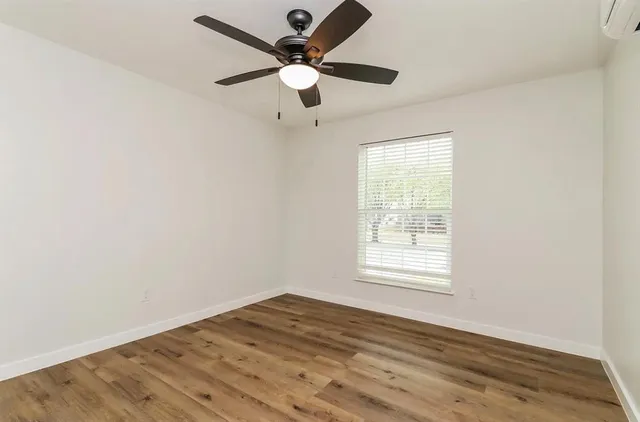 an empty room with wooden floor fan and windows