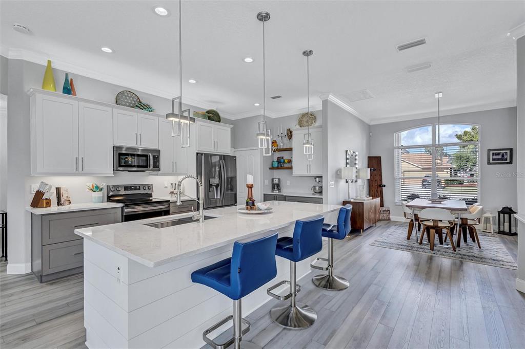 8409 29th Street East Parrish, FL 34219 - Photo 15 of 65 a kitchen with stainless steel appliances kitchen island granite countertop a stove a refrigerator a sink a dining table and chairs with wooden floor