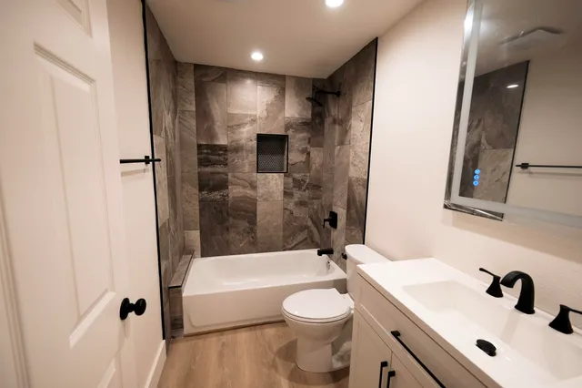 a bathroom with a bathtub shower sink vanity mirror and toilet