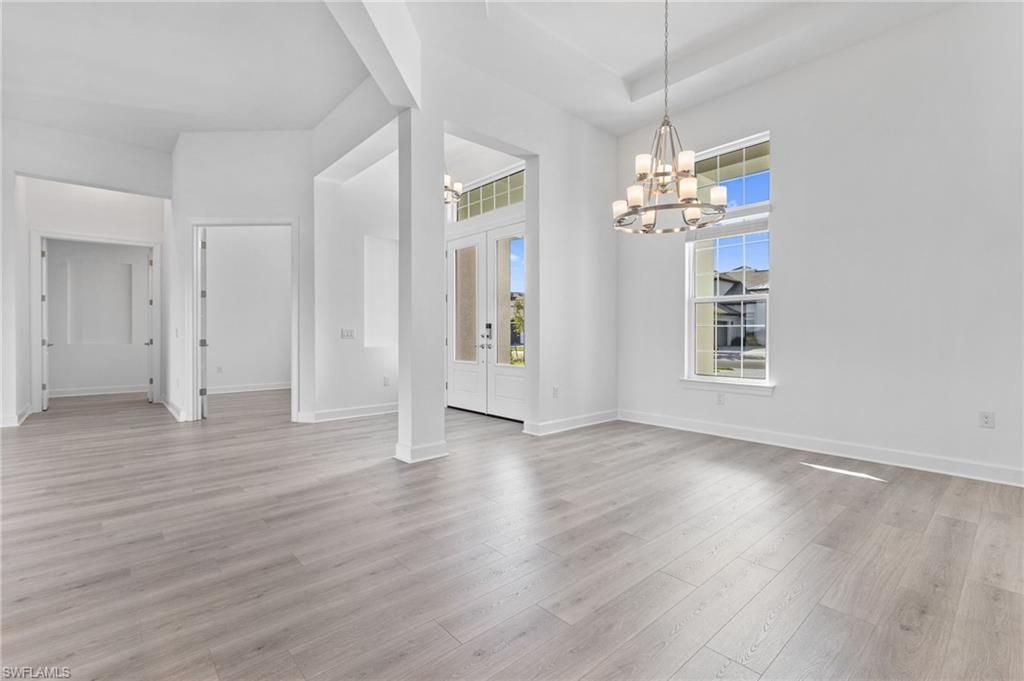 15564 Montello Lane Naples, FL 34114 - Photo 19 of 49 an empty room with wooden floor chandelier and windows