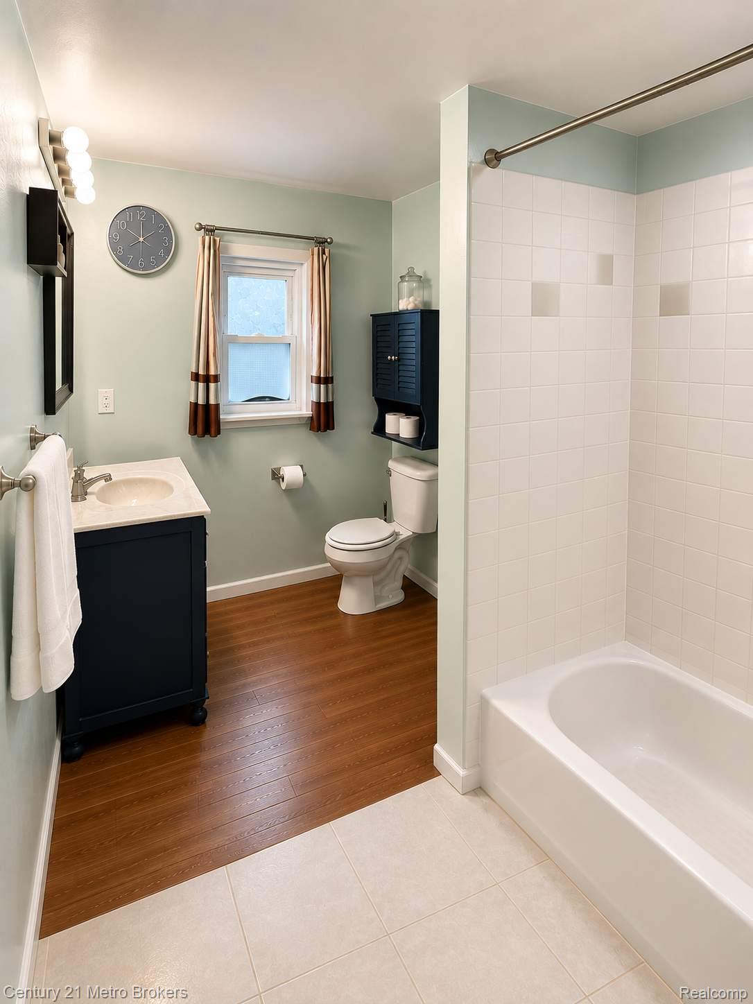 301 Field Road Clio, MI 48420 - Photo 9 of 32 Bathroom featuring a single vanity with a light-toned countertop, wood-finish flooring, and a white tiled shower/tub combination