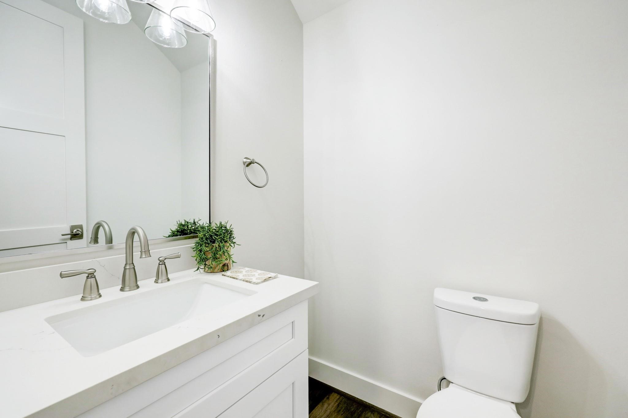 3827 Arlington Street Houston, TX 77018 - Photo 16 of 39 This is a modern, minimalist bathroom featuring a sleek white vanity with dual faucets, a large mirror, and a small plant for decor. The room has bright, clean lines with ample lighting.