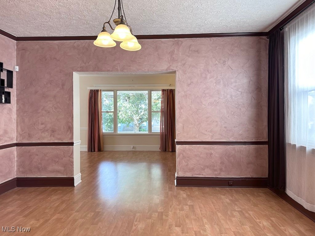 6846 Ottawa Road Cleveland, OH 44105 - Photo 10 of 50 Spare room featuring a textured ceiling, wood finished floors, wallpapered walls, and ornamental molding