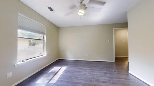 an empty room with wooden floor fan and windows
