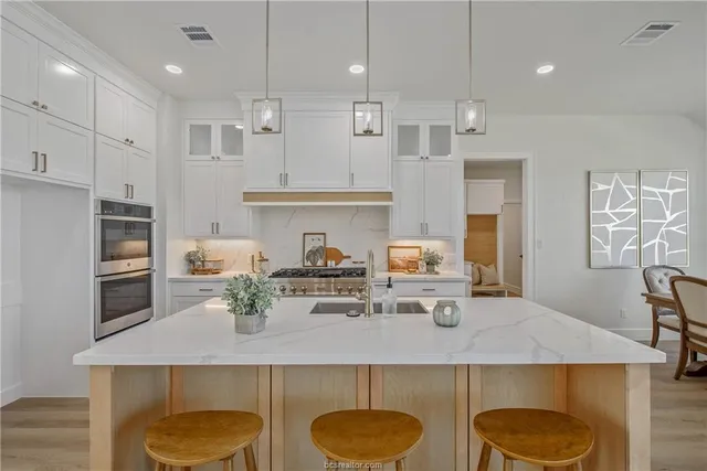 a kitchen with stainless steel appliances granite countertop a sink a stove a refrigerator and white cabinets