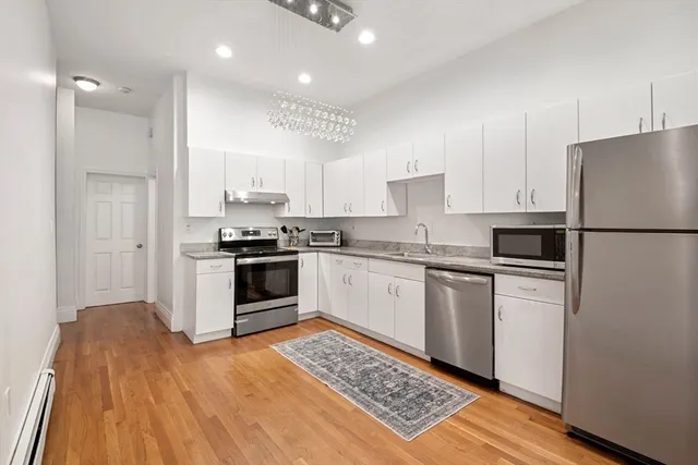 a kitchen with granite countertop a refrigerator oven a sink and white cabinets