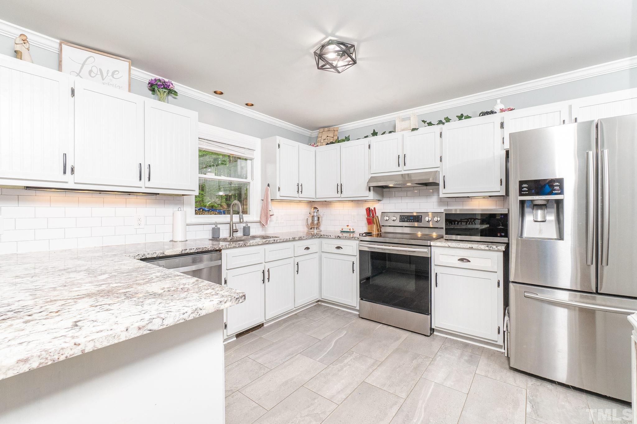 6313 Craig Road Durham, NC 27712 - Photo 21 of 38 a kitchen with granite countertop a refrigerator oven a sink and white cabinets