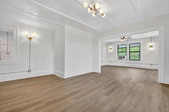 an empty room with wooden floor chandelier and windows