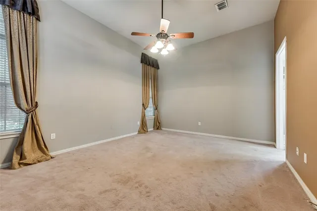 an empty room with a chandelier fan and windows