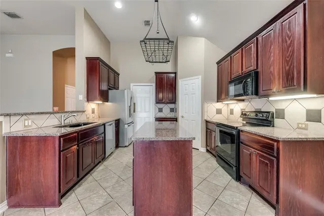 a large kitchen with stainless steel appliances granite countertop a stove top oven a sink dishwasher and a refrigerator with the cabinets