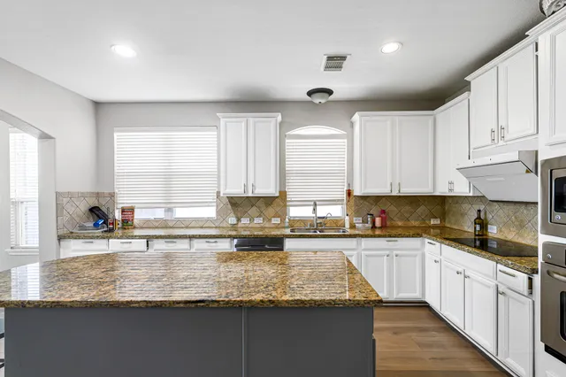 a kitchen with granite countertop a sink a counter top space cabinets and stainless steel appliances