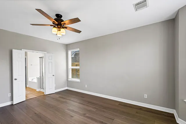 an empty room with wooden floor fan and windows