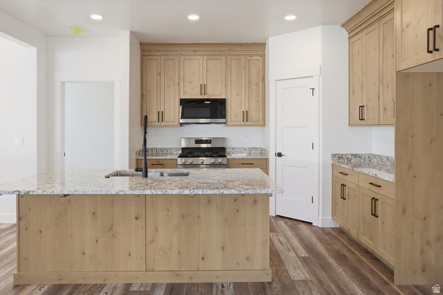 1315 West 3200 South, Unit 17 Perry, UT 84302 - Photo 12 of 58 Spacious kitchen featuring light wood cabinetry with black hardware, stone countertops, a large island with an undermount sink and matte black faucet, stainless steel appliances, and wood-finish flooring