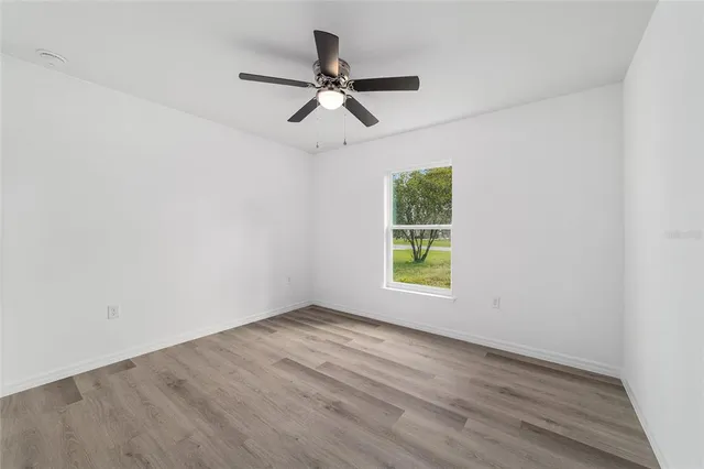 an empty room with wooden floor ceiling fan and window