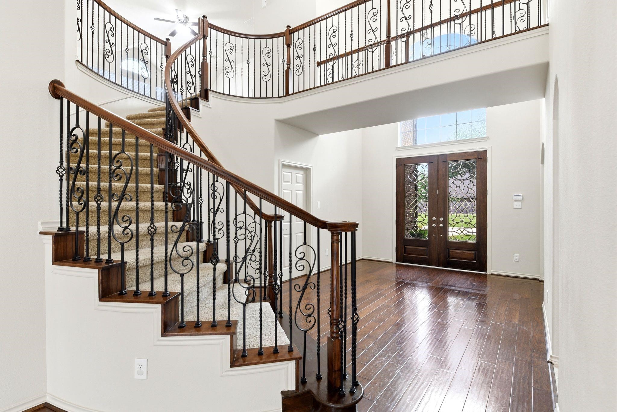 19903 Senterra Lakes Boulevard Spring, TX 77379 - Photo 5 of 50 Elegant entryway featuring a grand staircase with wrought iron railings, complemented by rich hardwood floors and a welcoming double-door entrance.