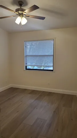 an empty room with wooden floor chandelier fan and windows