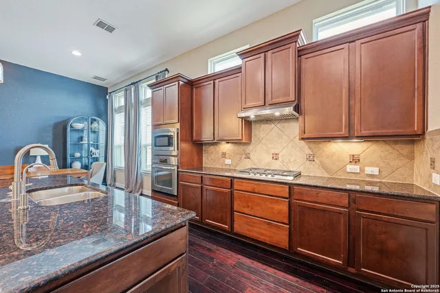 a kitchen with granite countertop stainless steel appliances a sink dishwasher refrigerator stove and cabinets