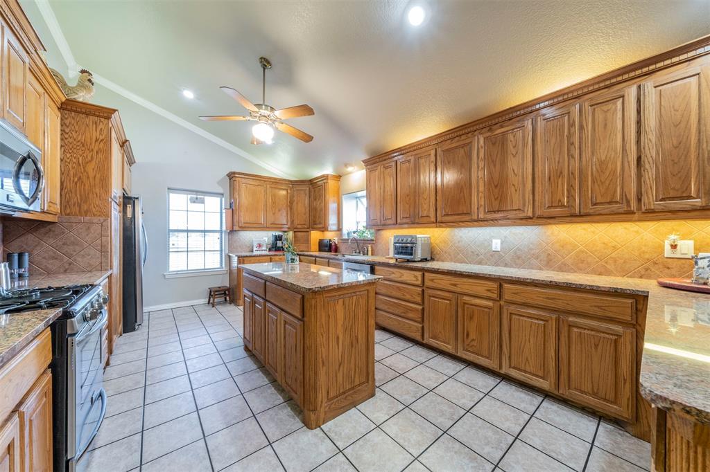 20175 Willow Glade Circle Pilot Point, TX 76258 - Photo 8 of 32 Kitchen with light stone countertops, a center island, stainless steel appliances, and vaulted ceiling