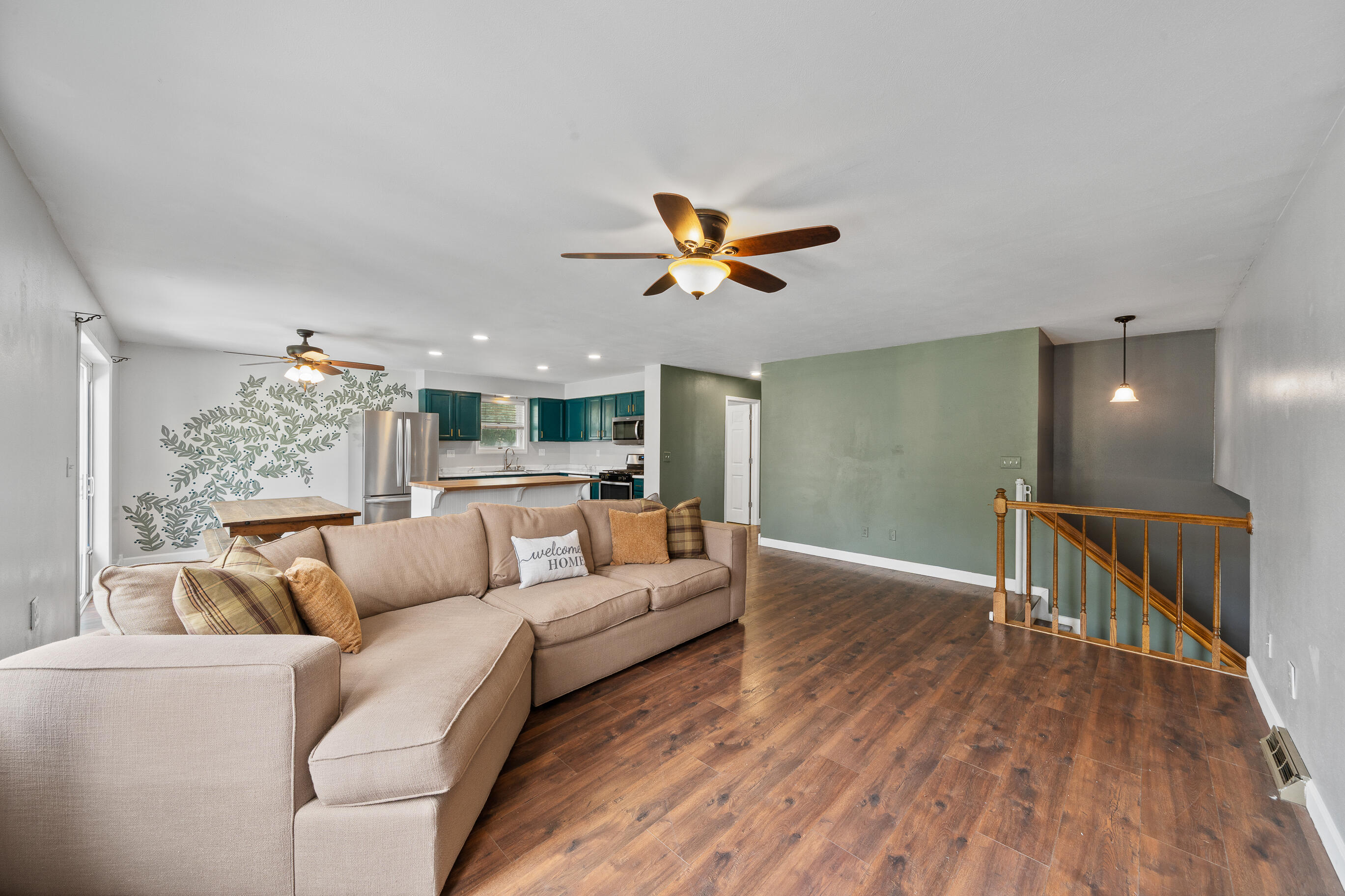 2212 Borg Road Delavan, WI 53115 - Photo 43 of 43 Open floor plan living area with ceiling fan, decorative leaf wall mural, teal kitchen cabinetry, and staircase to lower level with accent wall