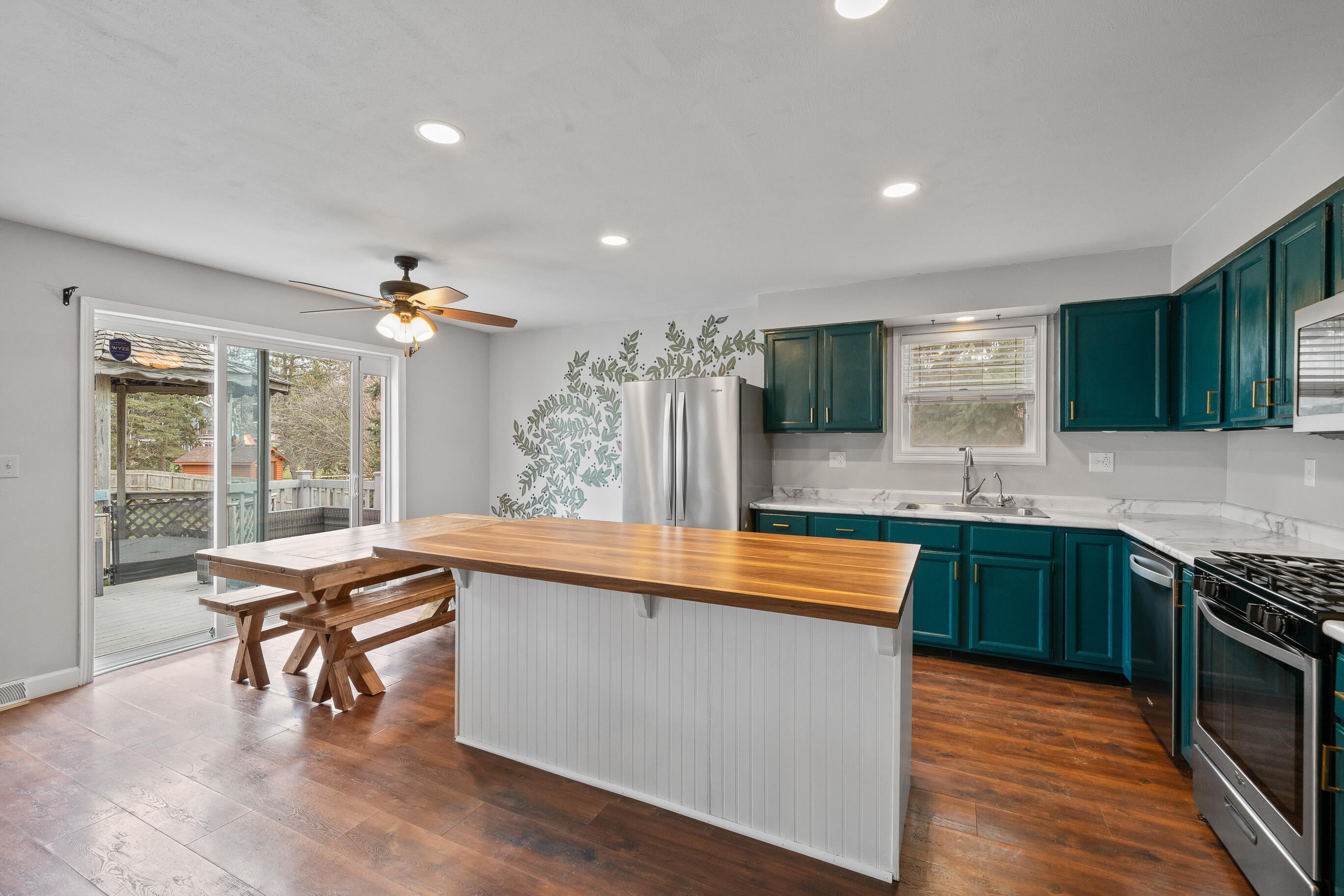 2212 Borg Road Delavan, WI 53115 - Photo 15 of 43 Kitchen and dining area with island, teal cabinetry, stainless steel appliances, decorative leaf wall mural, and sliding glass door to deck