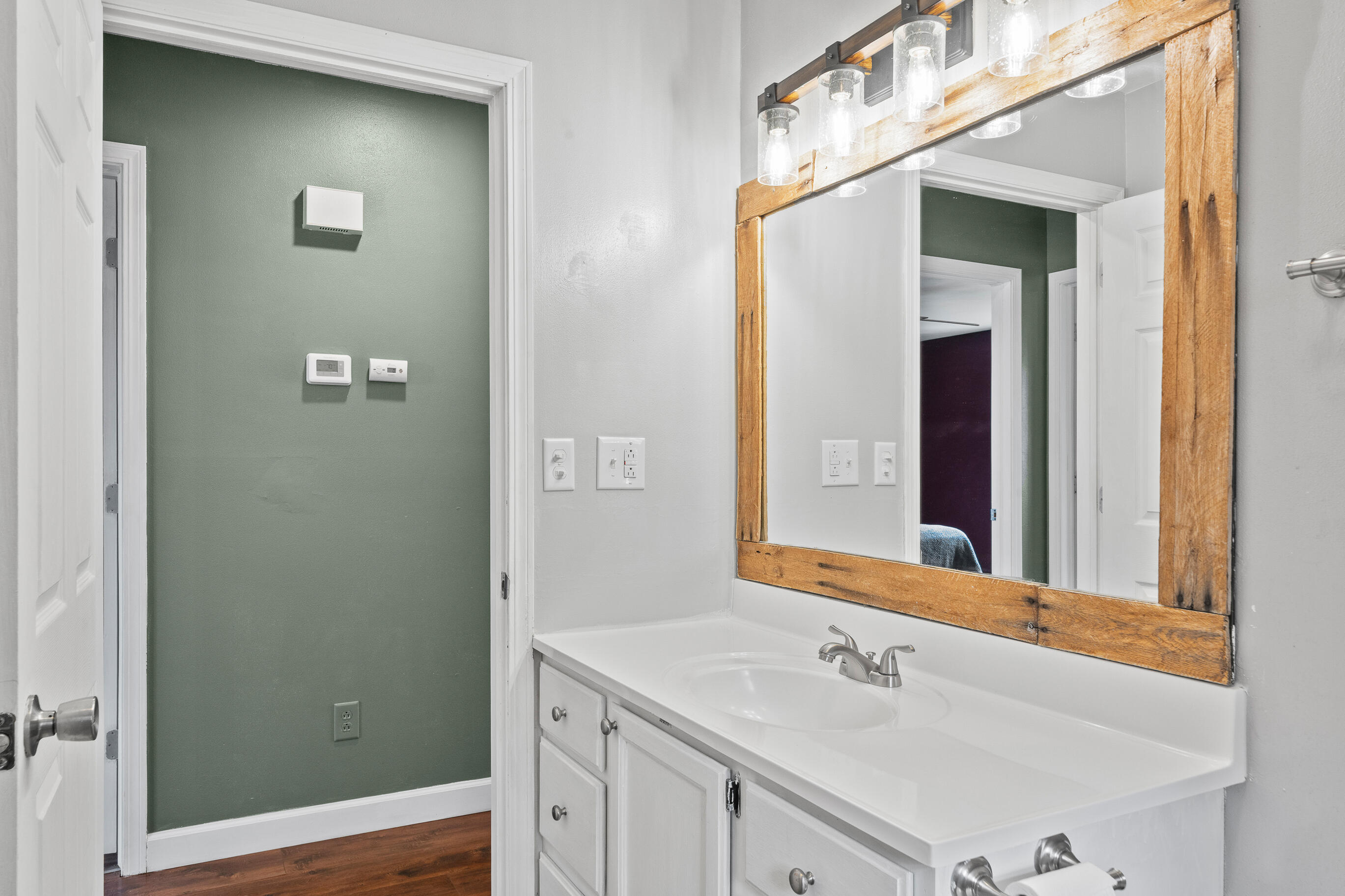2212 Borg Road Delavan, WI 53115 - Photo 24 of 43 Bathroom vanity detail with rustic wood-framed mirror, mason jar-style light fixture, and view into hallway with sage green accent wall and thermostat
