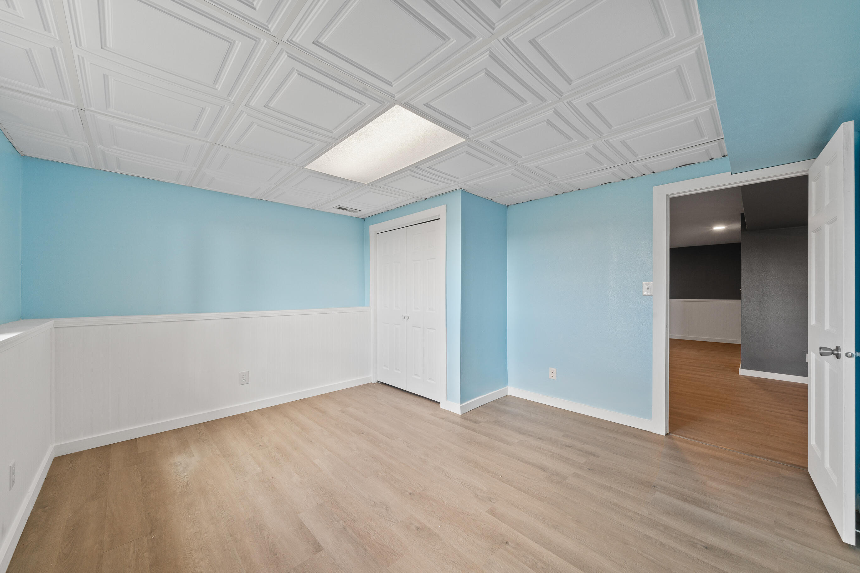 2212 Borg Road Delavan, WI 53115 - Photo 31 of 43 Lower level bedroom with light blue walls, white beadboard wainscoting, decorative ceiling tiles, bi-fold closet doors, and vinyl plank flooring
