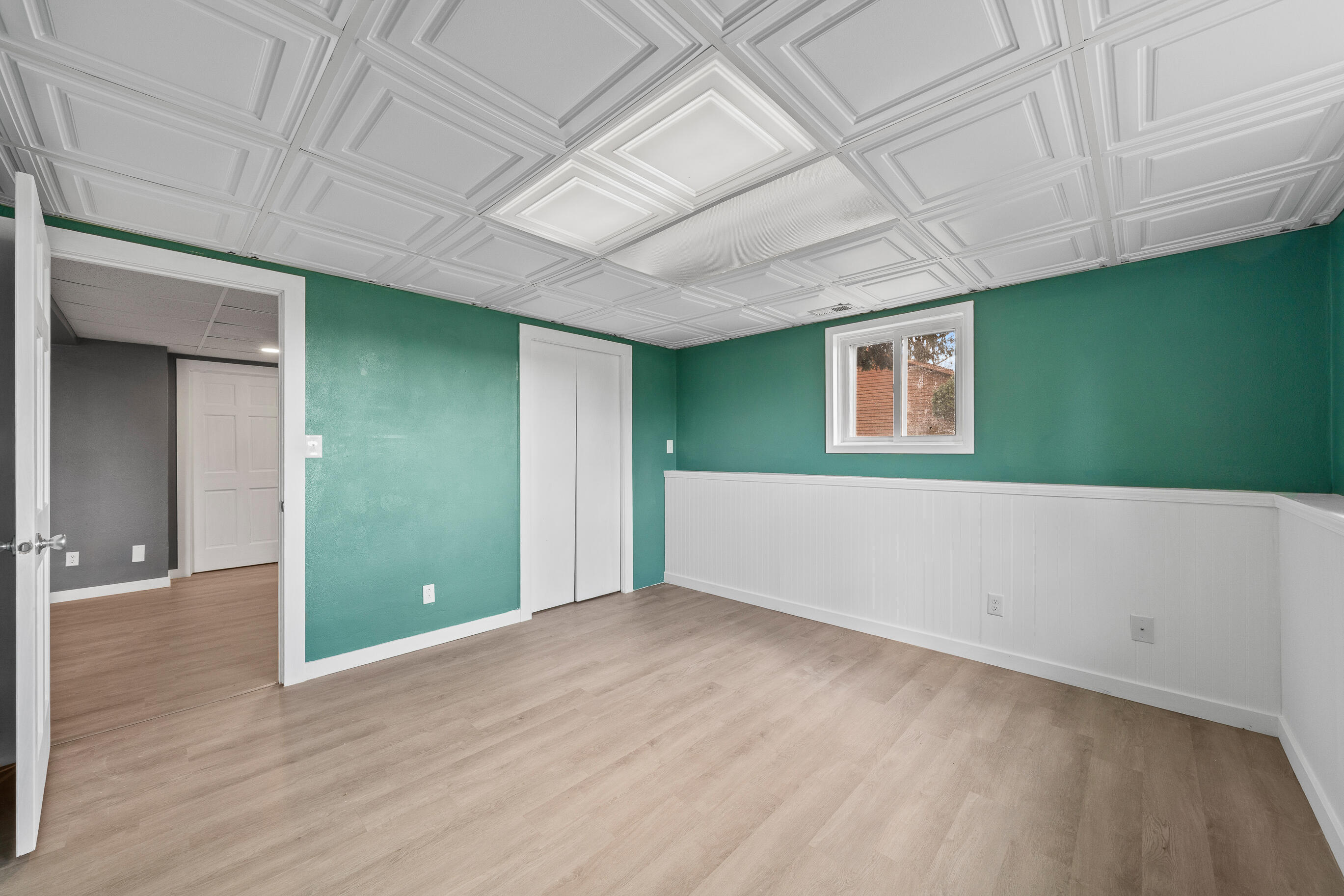 2212 Borg Road Delavan, WI 53115 - Photo 35 of 43 2nd Lower level bedroom with teal green walls, white beadboard wainscoting, decorative ceiling tiles, bi-fold closet doors, window, and vinyl plank flooring