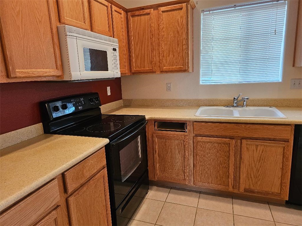 1069 Teddy Roosevelt Road Golden Valley, AZ 86413 - Photo 7 of 24 Kitchen with black appliances, light countertops, brown cabinetry, and light tile patterned flooring