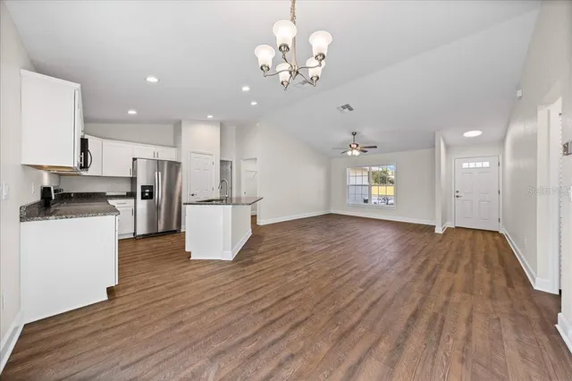 a view of an empty room and kitchen with wooden floor
