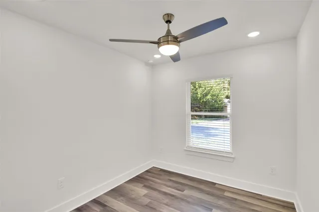 an empty room with wooden floor fan and windows