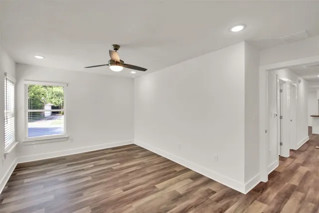 an empty room with wooden floor chandelier fan and windows