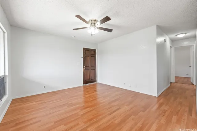 a view of an empty room with wooden floor and a ceiling fan