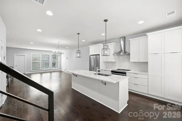 a large kitchen with stainless steel appliances granite countertop a stove a sink a refrigerator and white cabinets with wooden floor