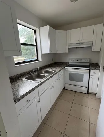 a kitchen with granite countertop white cabinets appliances a sink and a window