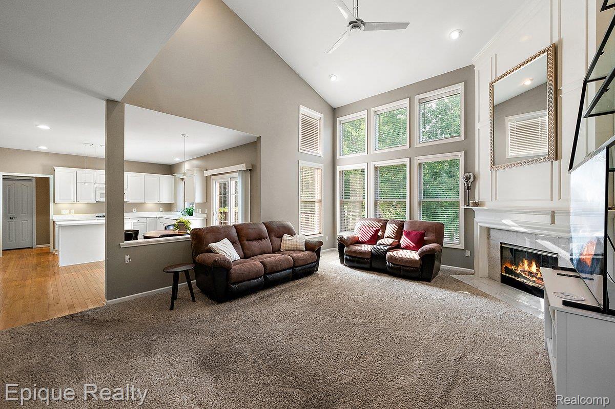 1909 Catlin Drive Rochester, MI 48306 - Photo 18 of 76 Vaulted ceiling living room featuring a gas fireplace with stone surround, a wall of windows, recessed lighting, and an open-concept design to the kitchen with white cabinetry and wood-finish flooring