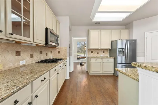 a kitchen with stainless steel appliances granite countertop a stove top oven a refrigerator a sink and dishwasher with white cabinets