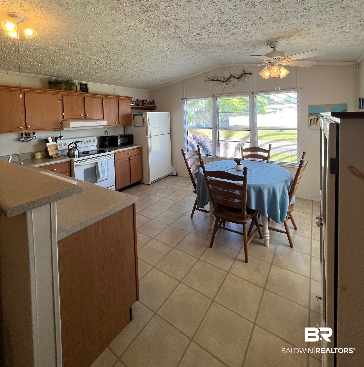 1936 Ridgewood Drive Lillian, AL 36549 - Photo 3 of 30 Kitchen with ceiling fan, white appliances, under cabinet range hood, brown cabinets, and lofted ceiling