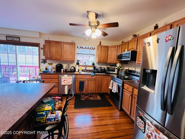 a kitchen with stainless steel appliances granite countertop a refrigerator a stove top oven a sink dishwasher and a dining table with wooden floor