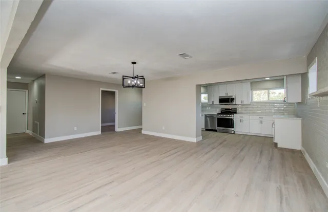 an empty room with wooden floor and kitchen view