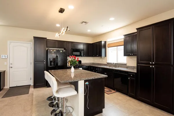 a kitchen with stainless steel appliances granite countertop a refrigerator a sink dishwasher a dining table and chairs with wooden floor