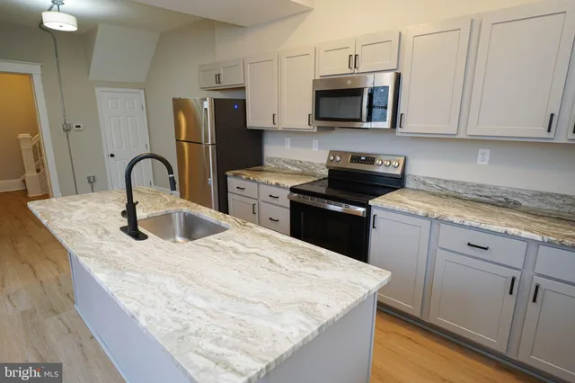 a kitchen with stainless steel appliances granite countertop a sink a stove top oven a refrigerator with white cabinets and wooden floor