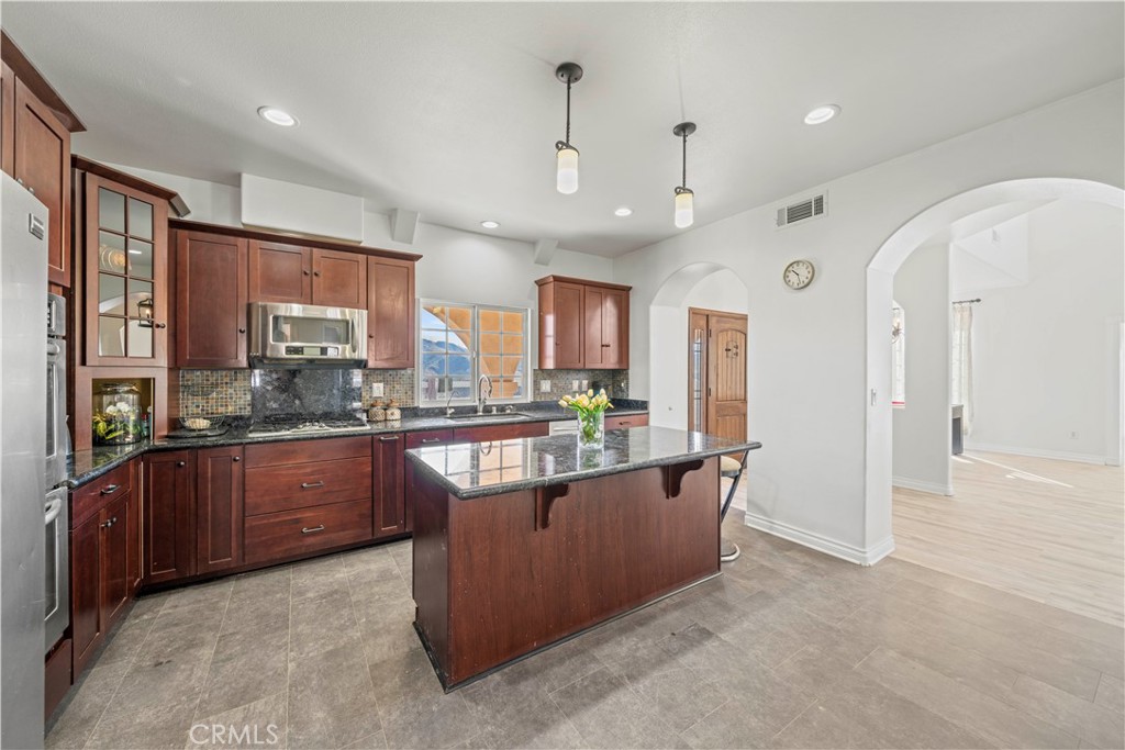 13560 Sego Road Agua Dulce, CA 91390 - Photo 24 of 75 a large kitchen with stainless steel appliances granite countertop a refrigerator a sink dishwasher a stove and a dining table with wooden cabinet