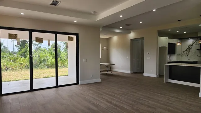 a view of an empty room with wooden floor and a kitchen
