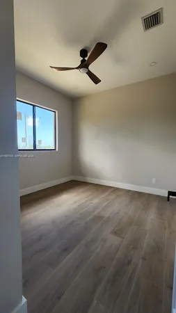an empty room with wooden floor fan and windows
